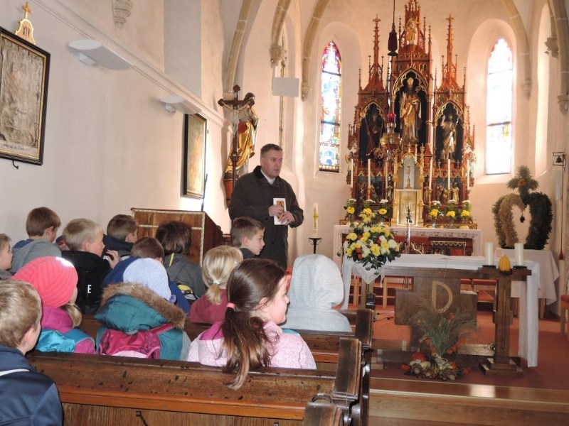 Der Pfarrer informiert die Kinder über die Pfarrkirche im Ort.